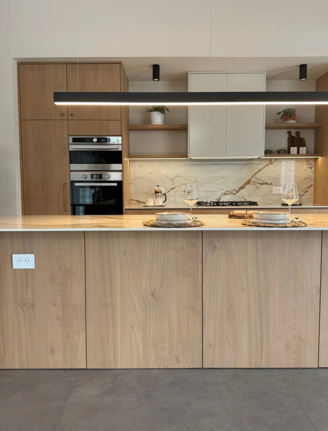Isla y frente de cocina con piedra veteada y muebles de madera clara
